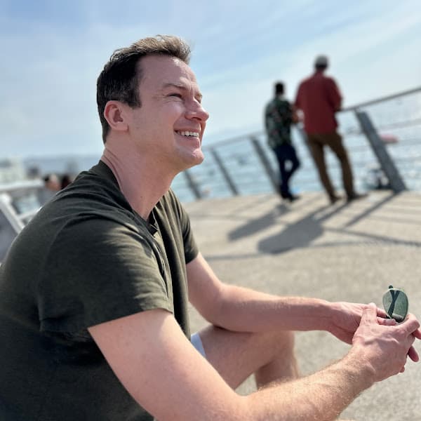 Aaron on a sunny pier, smiling and looking off-camera